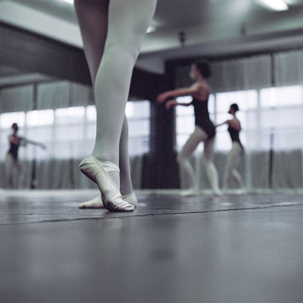 close-up of ballerina's legs in tights and ballet shoes on the dance floor with dancers blurred in the background. 