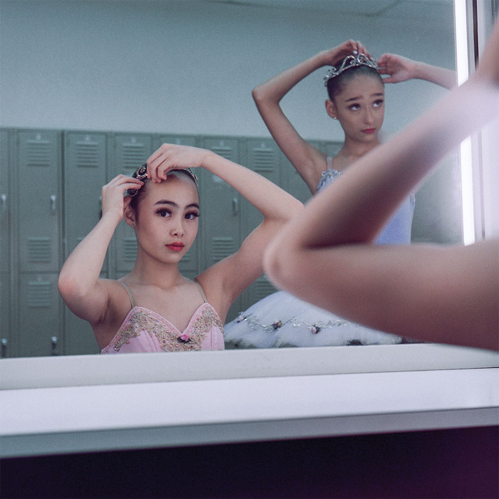 two young ballerinas fix their hair pins in front of the mirror in costume. 