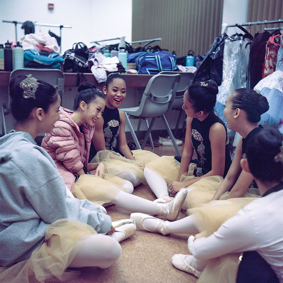 ballet dancers backstage sitting in a circle relaxed with sweatshirts and tutus. 