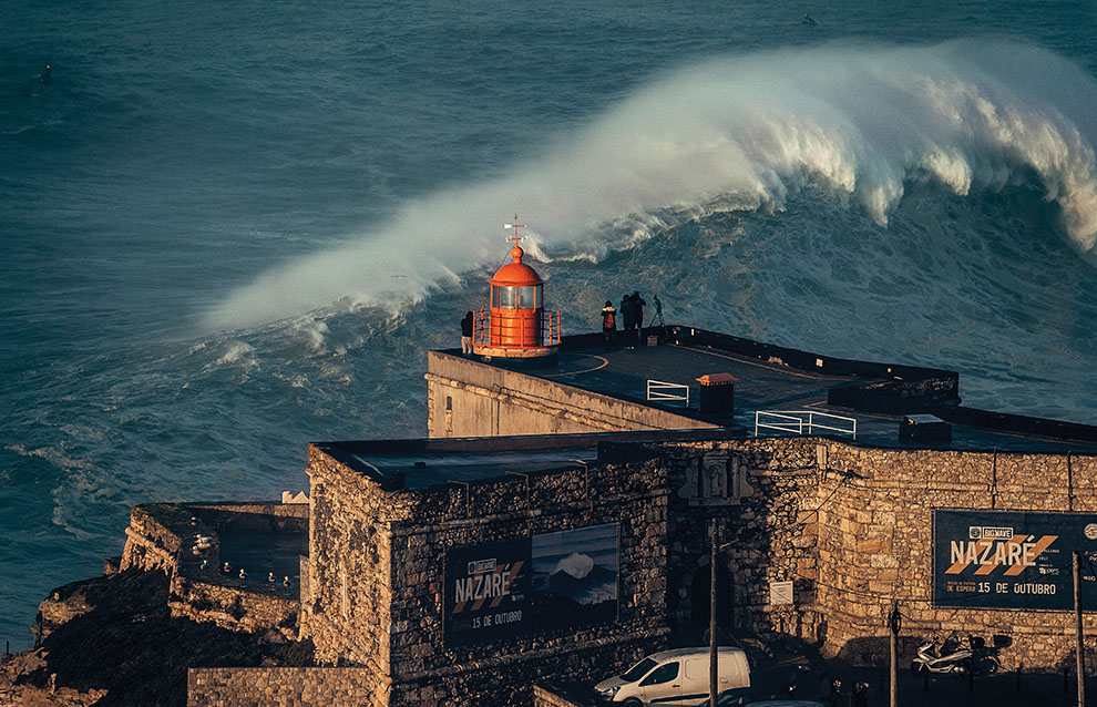 a large wave crashing at the edge near a light house
