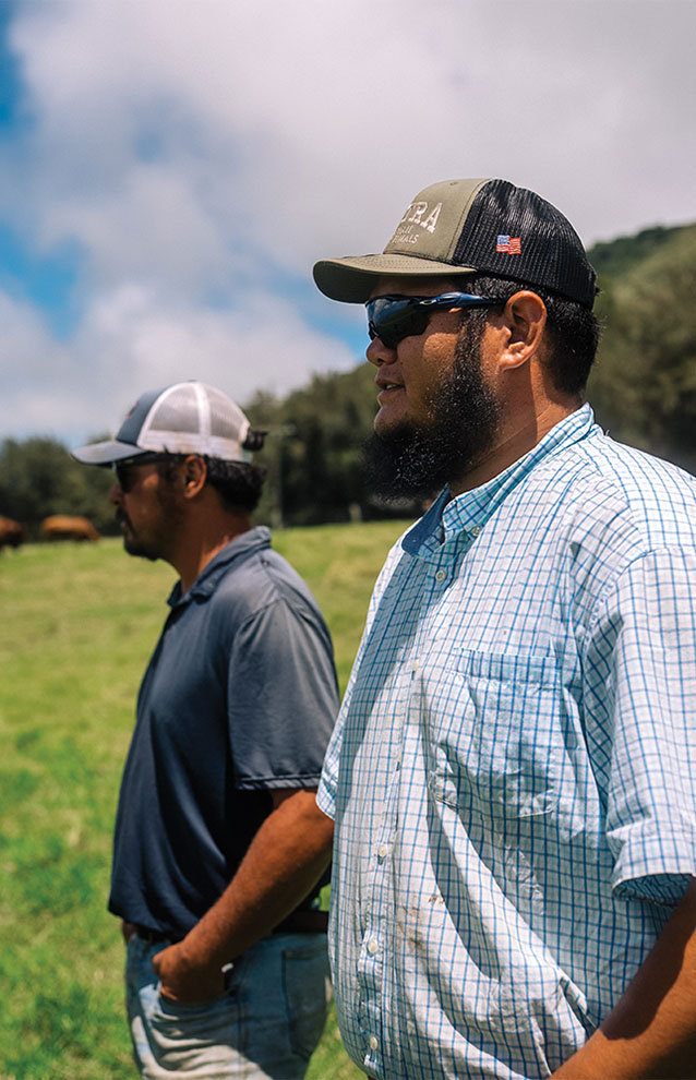 two ranch men outside with sunglasses in the green field with blue skies. 