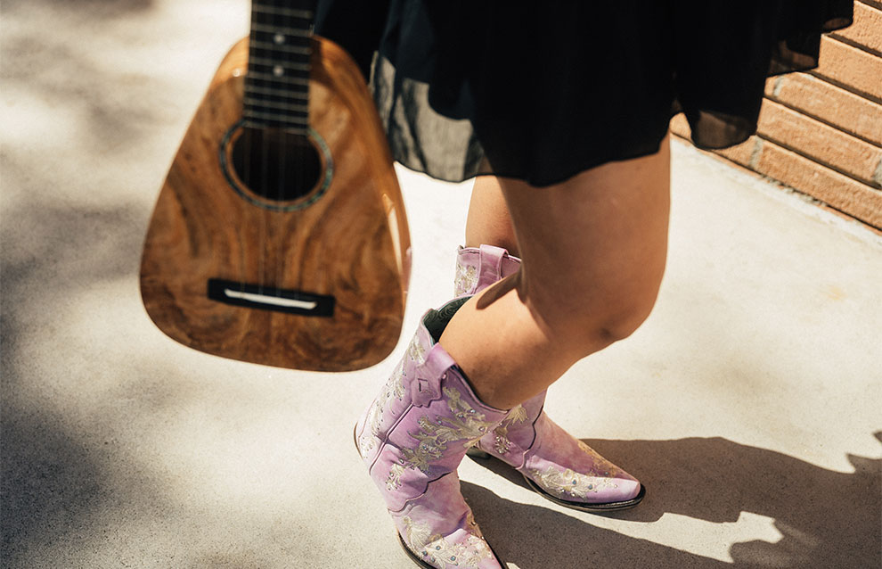close-up of person's legs holding string instrument and in pink cowboy boots 