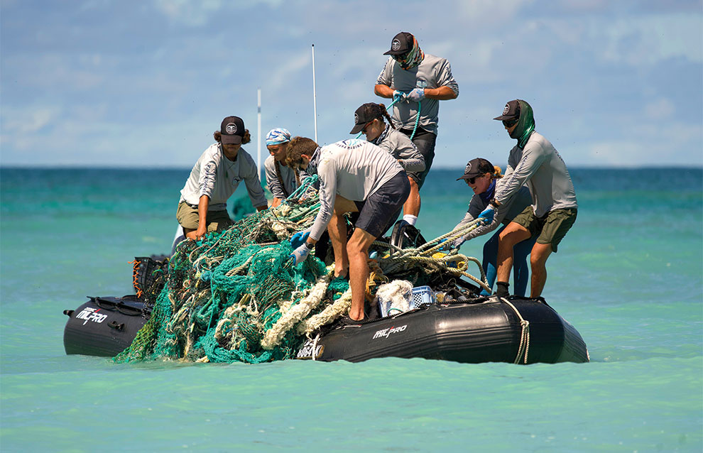 group of people on top of small raft dragging a blue net from the water onto the boat. 