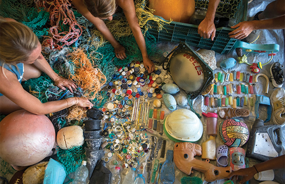 overhead shot of people gathered around collection of sea glass and trinkets pulled from the water. 