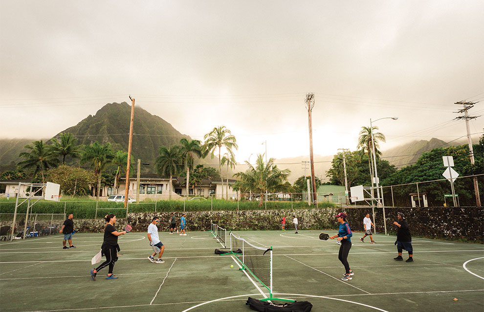 four pickleball players playing a game on green courts with luscious mountains in the background.