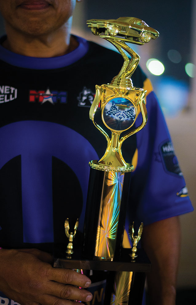 closeup of man in blue sporty shirt holding shiny trophy in arms.