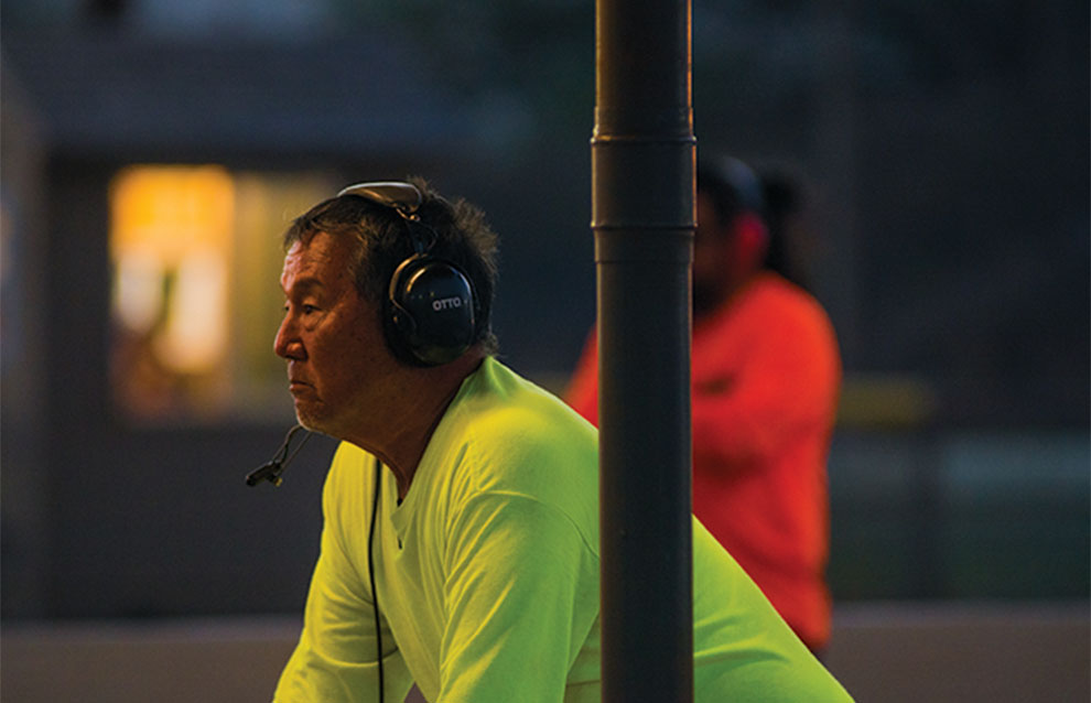 man in bright neon yellow shirt with headphones and a microphone attachment next to a pole