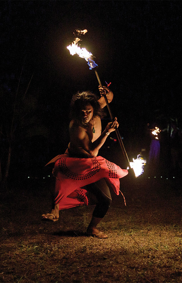 fire performer twirling batons in a red skirt at night. 