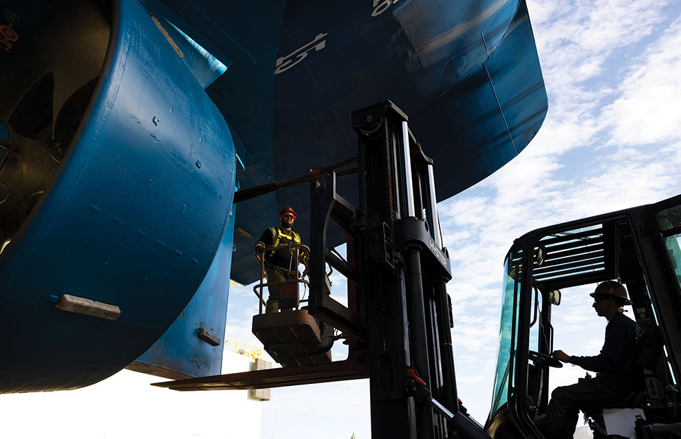 man operating crane next to the side of a giant blue ship. 