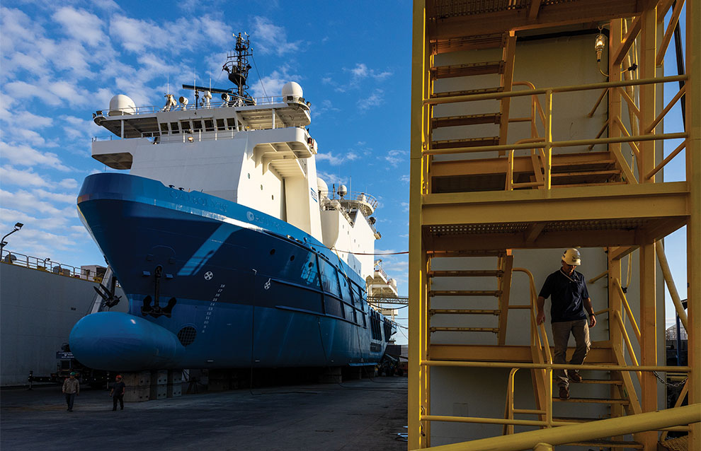 a massive blue boat docked next to an industrial yellow staircase for boarding. 
