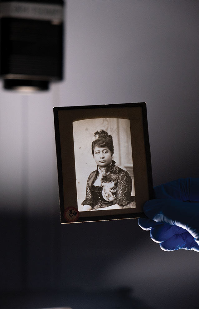 gloved hand holds black and white image of queen Liliuokalani. 