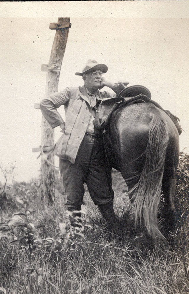 black and white photo of man in cowboy hat standing against his horse. 