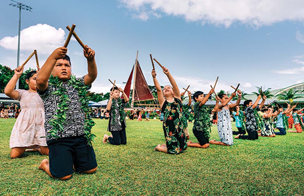 a group of children in hawaiian attire holding sticks